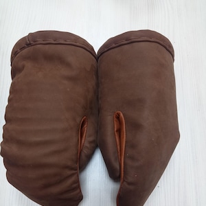 Puede incluir: Un par de guantes de horno de cuero marrón con forro marrón. Los guantes están hechos de un material grueso y duradero y tienen un puño largo.