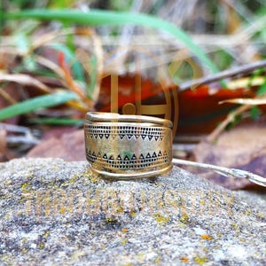 Peut inclure: Une bague en métal de couleur or avec un motif géométrique. La bague a une bande large.