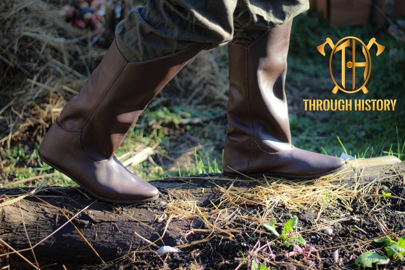May include: A pair of brown leather knee-high boots with a pointed toe. The boots are worn by a person walking on a log in a grassy area. The text "THROUGH HISTORY" is visible in the background.