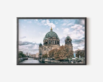 Puede incluir: Una impresión de arte mural enmarcada que muestra la Catedral de Berlín con su prominente cúpula verde y su ornamentada arquitectura de piedra. El edificio está situado a orillas de un río con árboles de colores otoñales bajo un cielo nublado.