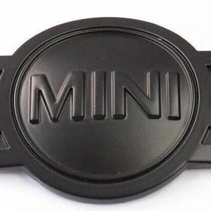 Peut inclure: Un emblème MINI noir mat avec des ailes. Le mot "MINI" est inscrit en lettres majuscules dans un cercle central. Les ailes s'étendent vers l'extérieur, avec des lignes détaillées. Finition mate.