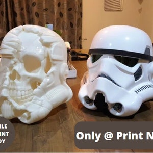May include: Two 3D printed helmets, one a skull and the other a Stormtrooper helmet, are shown on a wooden surface. The text "STL FILE 3D PRINT READY" is in a white circle on the left side of the image. The text "Only @ Print Noble" is in a black rectangle on the right side of the image.