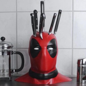May include: A red and black Deadpool-themed knife block holding several black-handled knives. The knife block is shaped like Deadpool's mask. A stainless steel French press and a faucet are also visible.