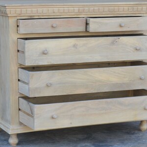 Puede incluir: Una c&oacute;moda de madera clara con cinco cajones. Los cajones est&aacute;n abiertos, revelando el interior de madera. La c&oacute;moda tiene una parte superior decorativa y patas torneadas.
