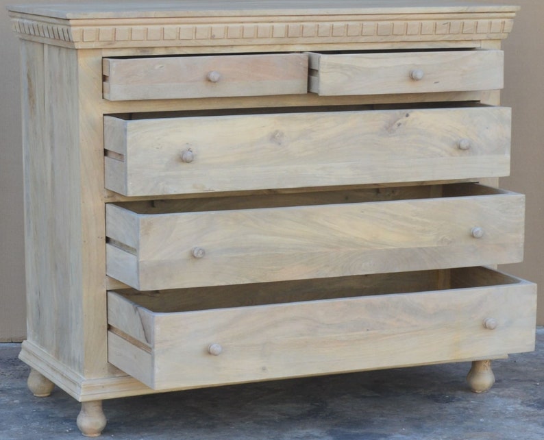 Puede incluir: Una c&oacute;moda de madera clara con cinco cajones. Los cajones est&aacute;n abiertos, revelando el interior de madera. La c&oacute;moda tiene una parte superior decorativa y patas torneadas.