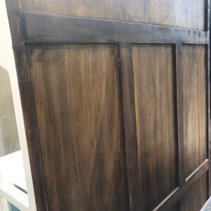 May include: Close-up of a wooden cabinet door with a dark brown stain. The door is made of several panels with raised edges.