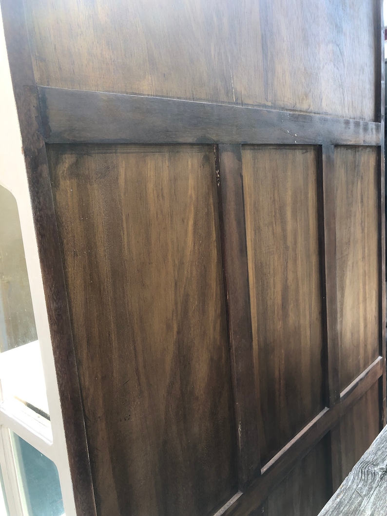 May include: Close-up of a wooden cabinet door with a dark brown stain. The door is made of several panels with raised edges.