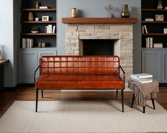 May include: A brown leather bench with a grid pattern sits in front of a brick fireplace. The bench has a black metal frame and is placed on a light-colored rug. Bookshelves are on either side.