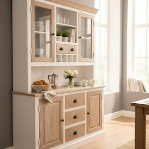May include: A two-toned wooden hutch with glass-fronted upper cabinets and solid lower cabinets. The hutch features a light wood trim and drawer fronts, with white painted surfaces. The top section has glass doors, and the bottom section has solid doors and drawers.