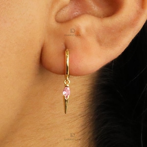 May include: Gold hoop earrings with a pink gemstone dangling from the bottom. The gemstone is shaped like a teardrop and is set in a gold setting.