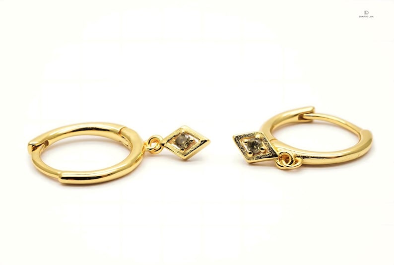 Pode incluir: Um par de brincos de argola de ouro com um pingente em forma de diamante. Cada pingente apresenta uma pequena gema transparente no centro.