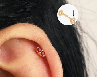 Könnte beinhalten: Nahaufnahme eines Ohres mit einem goldenen Helix-Piercing mit drei roten Edelsteinen.