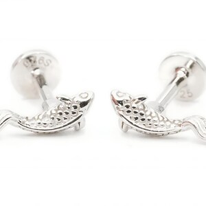 May include: A pair of silver fish stud earrings. The fish are detailed with a textured surface and have a silver post and butterfly backing.