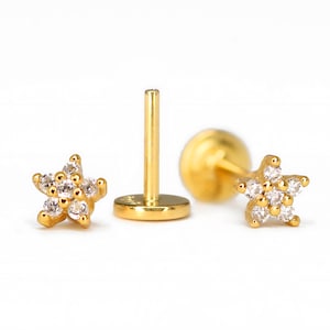 May include: A pair of gold star-shaped earrings with clear cubic zirconia stones. The earrings are on a white background.