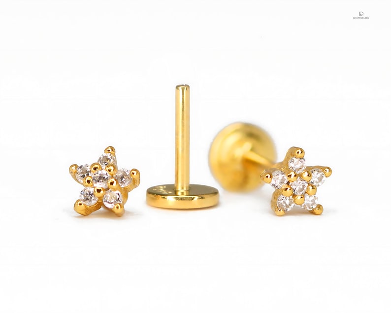 May include: A pair of gold star-shaped earrings with clear cubic zirconia stones. The earrings are on a white background.