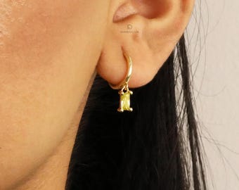 Puede incluir: Aretes de aro de oro con un colgante de piedra preciosa amarilla. La piedra preciosa tiene forma rectangular.