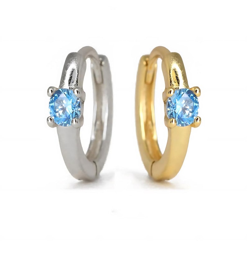 K&ouml;nnte beinhalten: Ein Paar Creolen mit einem kleinen blauen Edelstein, der in jedem Creolen sitzt. Ein Creolen ist silber und der andere ist gold.