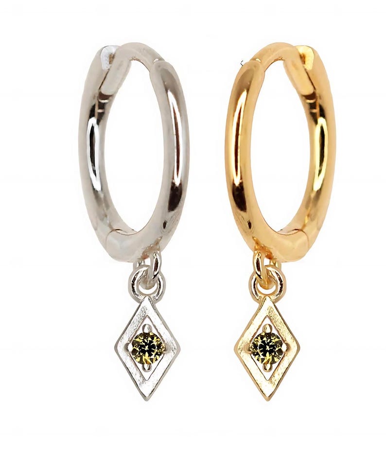 Pode incluir: Um par de brincos de argola com um pingente em forma de diamante que apresenta uma pequena gema verde. Um brinco &eacute; de prata e o outro &eacute; de ouro.
