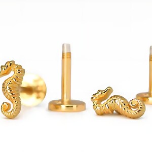 K&ouml;nnte beinhalten: Goldfarbener K&ouml;rperschmuck in Form eines Seepferds mit einem Stift und einer flachen R&uuml;ckseite. Das Seepferdchen ist mit strukturierten Schuppen verziert.