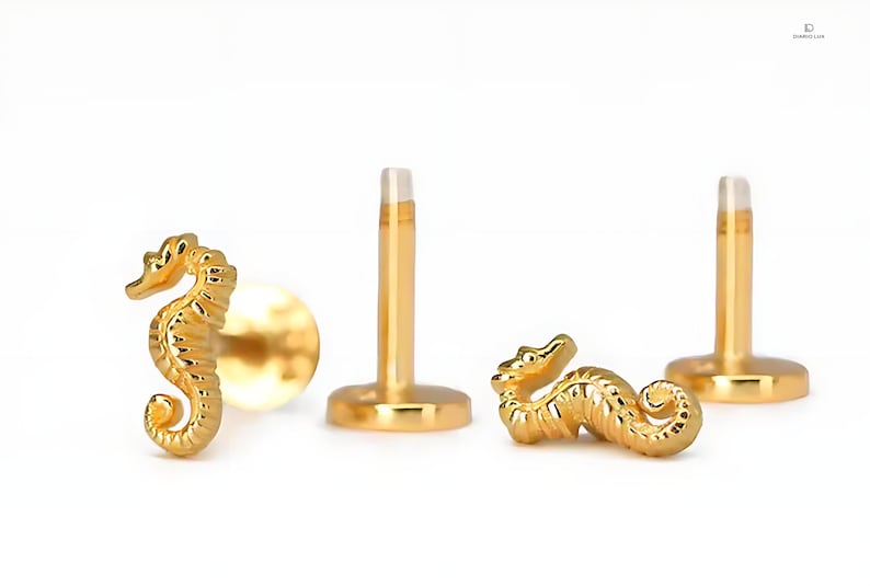 K&ouml;nnte beinhalten: Goldfarbener K&ouml;rperschmuck in Form eines Seepferds mit einem Stift und einer flachen R&uuml;ckseite. Das Seepferdchen ist mit strukturierten Schuppen verziert.