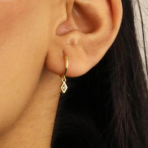 May include: Gold hoop earrings with a small diamond-shaped pendant hanging from each hoop.