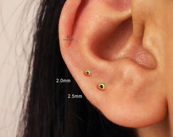 May include: Close-up of a person's ear with two gold ball earrings. The earrings are 2.0mm and 2.5mm in size.