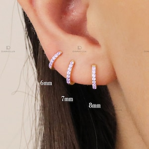 May include: Three gold hoop earrings with a row of small purple cubic zirconia stones. The hoops are 6mm, 7mm, and 8mm in diameter.