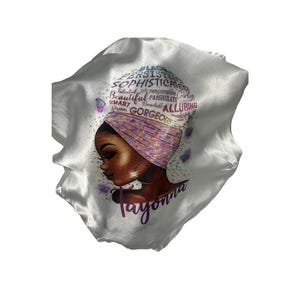 May include: White satin sleep cap with a colorful illustration of a woman with a headscarf and the words "Black, Persistent, Sophisticated, Talented,  Responsible,  Girl, Beautiful, Passionate, Smart,  Remarkable, Alluring,  Brave, Gorgeous,  Wonderful,  Tayonna".