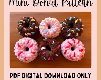 May include: Six crocheted mini donuts in various colors, including pink, brown, and blue. The donuts have white and colored sprinkles. The donuts are arranged on a wooden surface. The text "Mini Donut Pattern" is at the top of the image and "PDF DIGITAL DOWNLOAD ONLY" is at the bottom of the image.