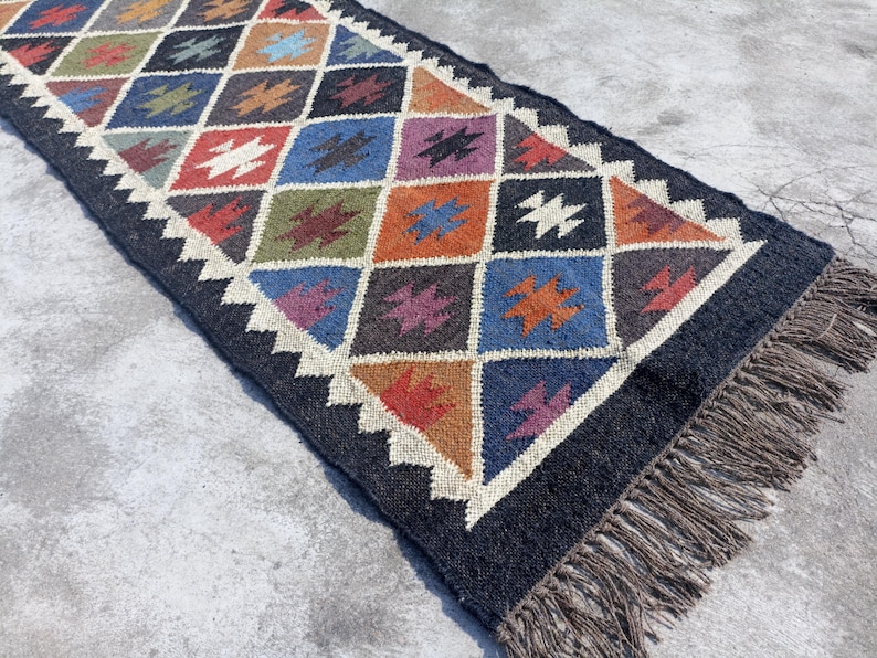 May include: A black and white geometric patterned rug with colourful accents. The rug has a fringe border and is made of wool.