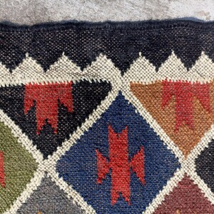 May include: A colourful geometric patterned rug with a black background. The rug is made of woven jute and features a variety of colours, including red, green, blue, and brown.