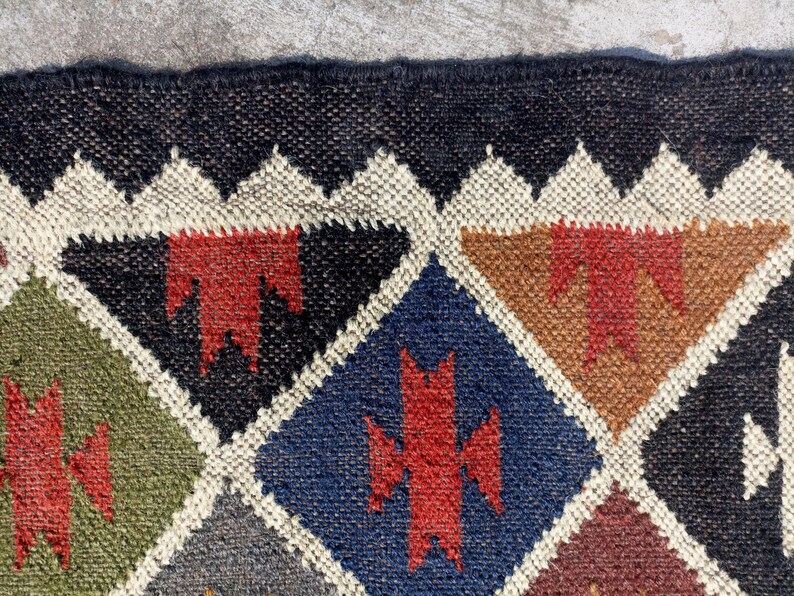 May include: A colourful geometric patterned rug with a black background. The rug is made of woven jute and features a variety of colours, including red, green, blue, and brown.