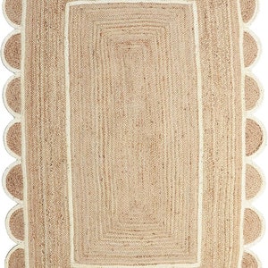 May include: A rectangular jute rug with a scalloped edge. The rug has a natural tan colour with a cream-coloured border and a rectangular design in the centre. The rug's dimensions are not visible.