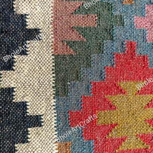 May include: A close-up of a colorful woven rug with geometric patterns in shades of red, blue, green, brown, and beige. The rug is made of natural fibers and has a textured surface.
