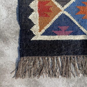 May include: A black and brown geometric patterned rug with fringe. The rug has a black background with brown, red, blue, and purple geometric shapes.