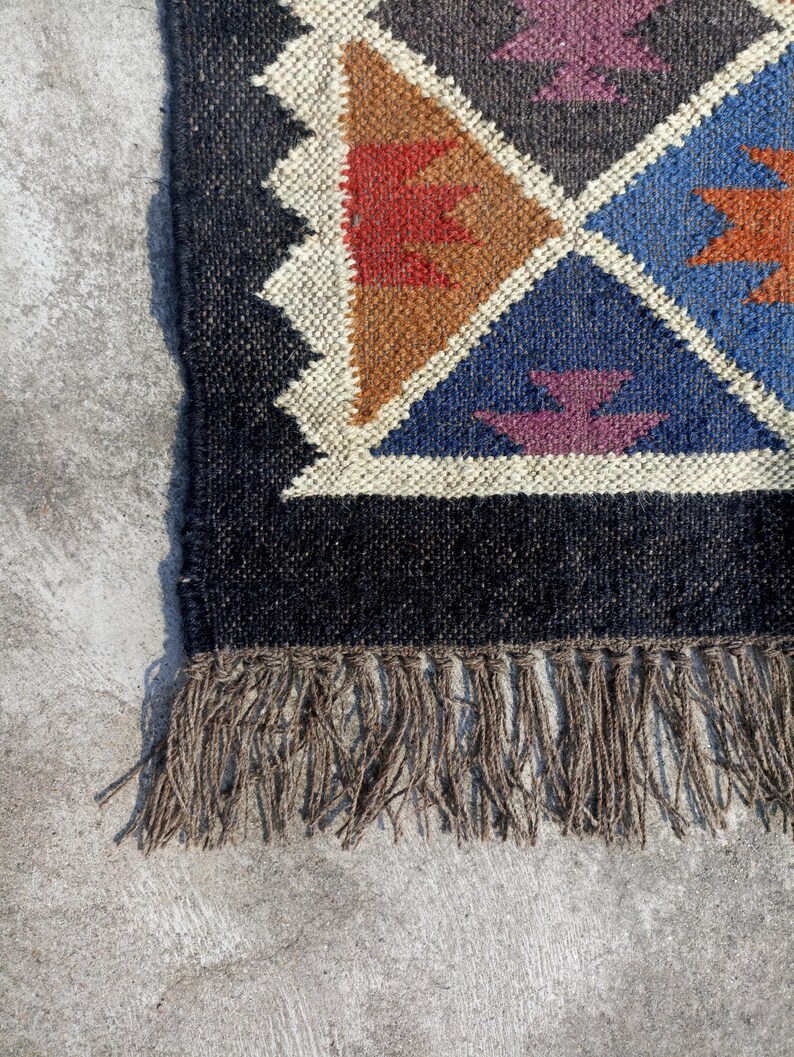 May include: A black and brown geometric patterned rug with fringe. The rug has a black background with brown, red, blue, and purple geometric shapes.