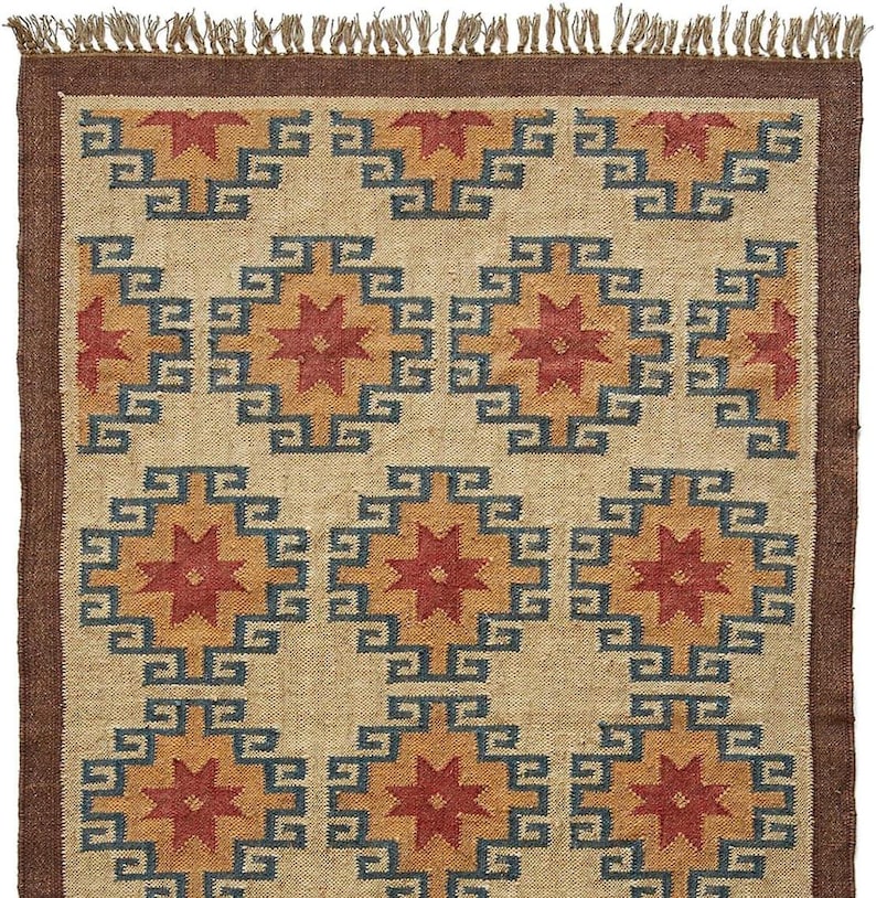 May include: A beige rug with a geometric pattern of red, orange, and blue stars. The rug has a brown fringe border.