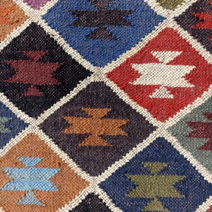 May include: A colourful diamond-shaped patterned rug with various shades of blue, red, brown, and white. The rug has a geometric design with a woven texture.