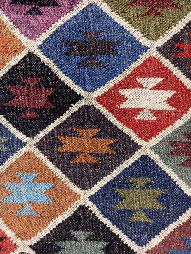 May include: A colourful diamond-shaped patterned rug with various shades of blue, red, brown, and white. The rug has a geometric design with a woven texture.