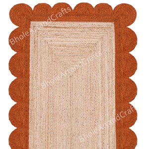 May include: A rectangular jute rug with a scalloped edge. The rug has a natural beige centre and a rust-coloured border. The text "Bhole WoodCrafts" is visible on the rug. Ideal for home decor.