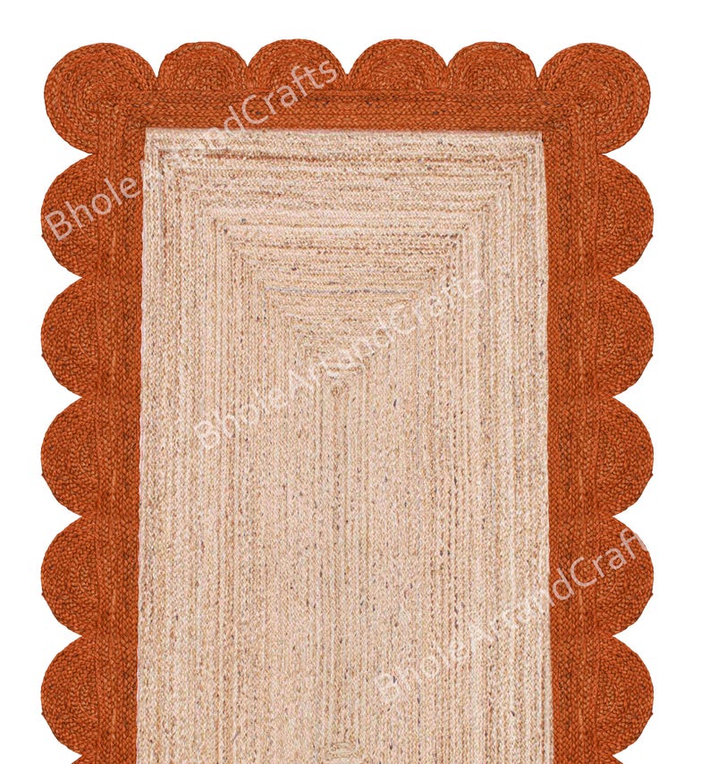 May include: A rectangular jute rug with a scalloped edge. The rug has a natural beige centre and a rust-coloured border. The text "Bhole WoodCrafts" is visible on the rug. Ideal for home decor.