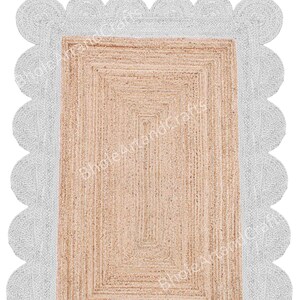 May include: Rectangular jute rug with a light brown centre and a white scalloped border. The rug has a woven texture and a neutral colour palette, suitable for various interior styles. The rug is designed for indoor use.