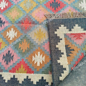May include: Multicolored geometric patterned rug with a black border and fringe. The rug is made of jute and is handwoven. The rug is folded in half, showing the back side of the rug.