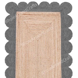 May include: A rectangular jute rug with a scalloped grey border. The centre of the rug is a natural beige colour, and the border is a darker grey. The text "Bhole AnandCrafts" is printed on the rug.