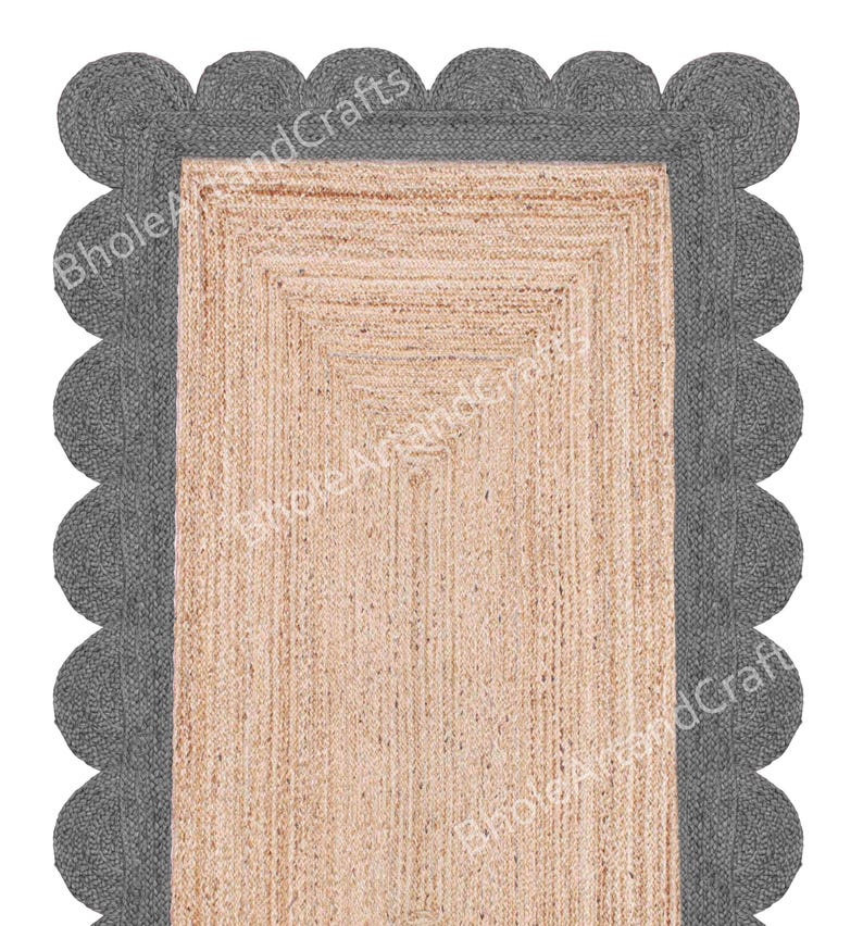 May include: A rectangular jute rug with a scalloped grey border. The centre of the rug is a natural beige colour, and the border is a darker grey. The text "Bhole AnandCrafts" is printed on the rug.