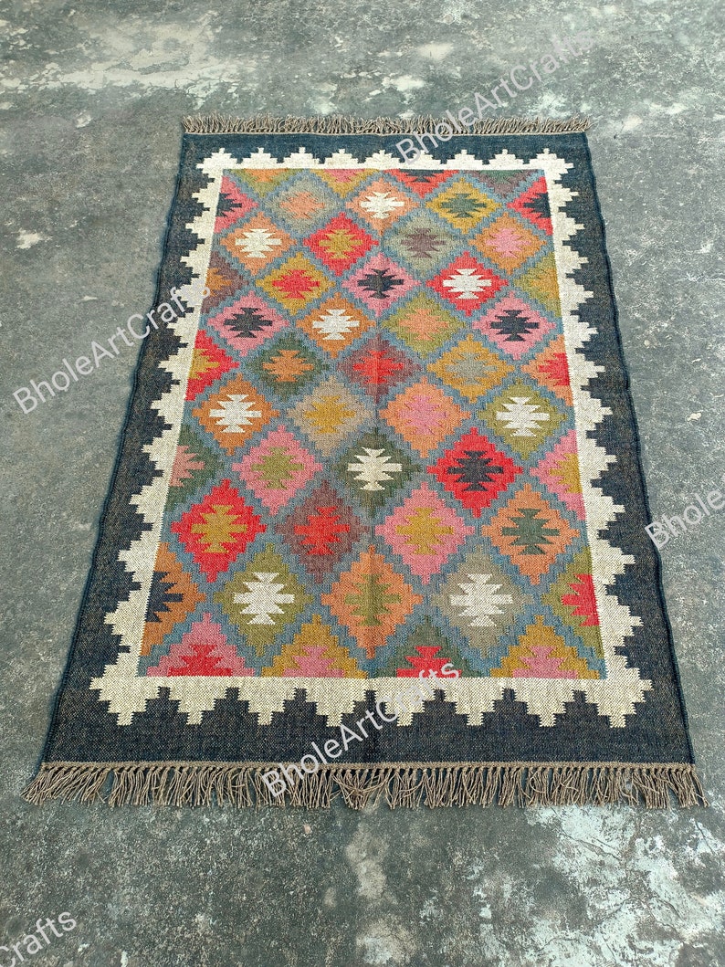 May include: A colorful, geometric patterned rug with a black border and fringe. The rug is made of wool and has a traditional design.