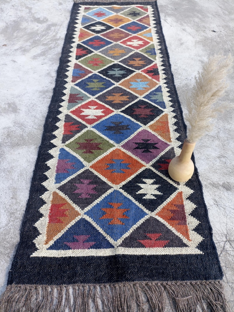 May include: A colourful, geometric patterned rug with a black background and fringe on the ends. The rug is made of wool and has a traditional design.