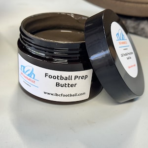 Może przedstawiać: Brązowy słoik z czarną pokrywką zawierający ciemnobrązową substancję. Słoik jest oznaczony etykietą "Football Prep Butter" i "www.lbcfootball.com".