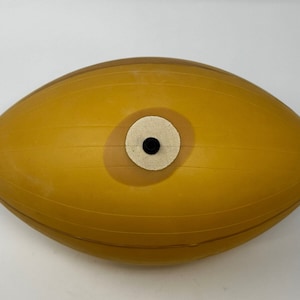 Peut inclure: Un ballon gonflable de forme ovale jaune avec un cercle blanc et un trou noir au centre.