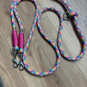 May include: A multi-coloured dog lead with a rainbow pattern. The lead has a braided rope design with a vibrant mix of pink, blue, yellow, and green. It has two bright pink handles and silver metal clasps.